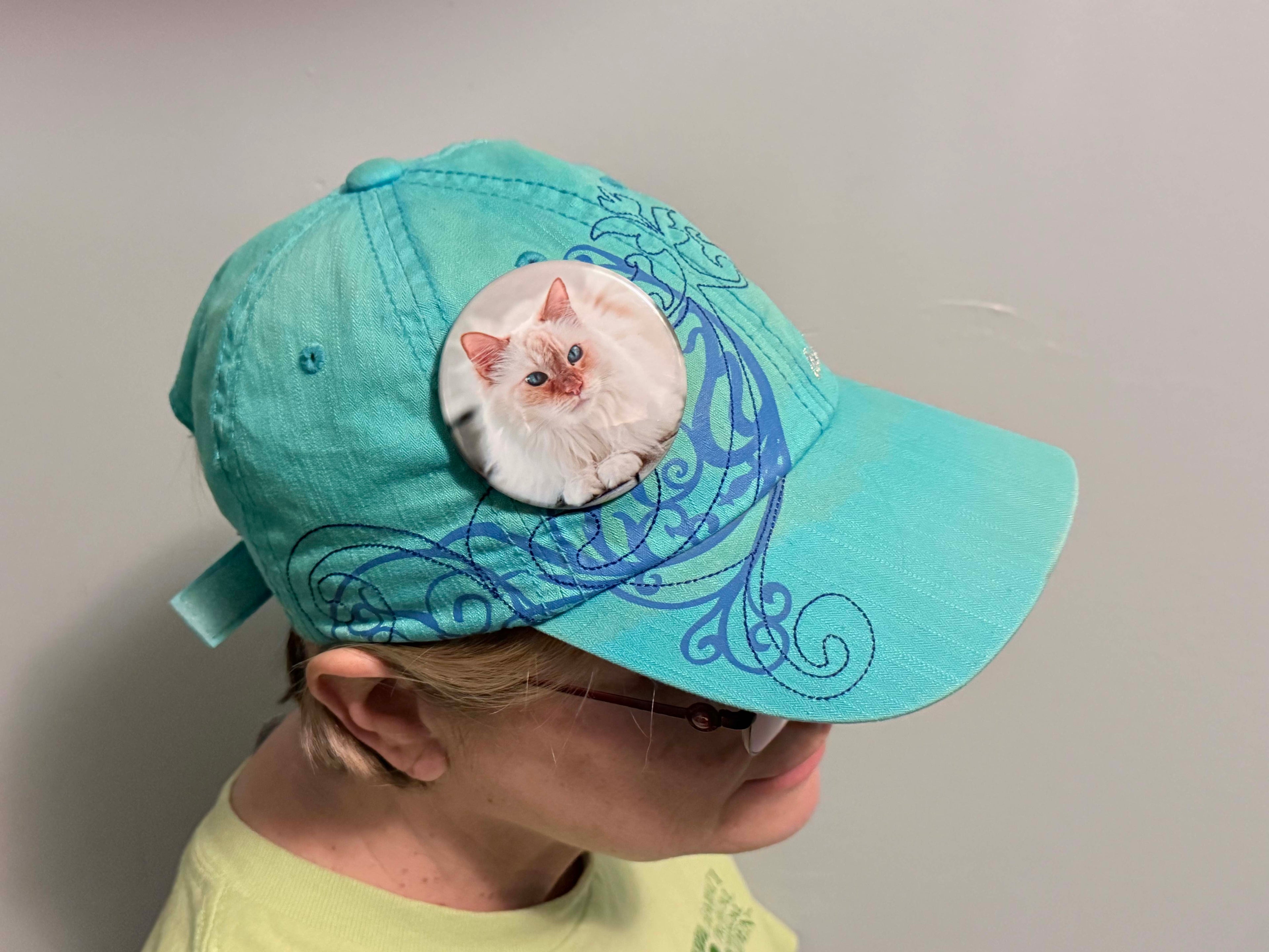 Woman wearing a teal cap with a cat design on a plain background