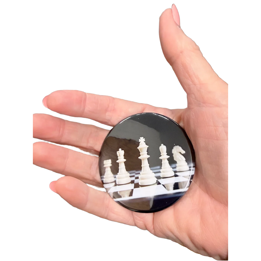 Hand holding a round magnet with chess pieces on a chessboard